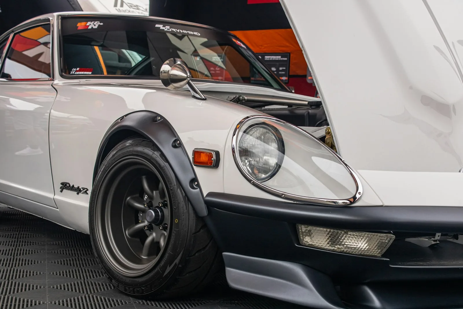 Přední část bílého kupé Datsun Fairlady Z s otevřenou kapotou a rozšířenými blatníky na výstavě